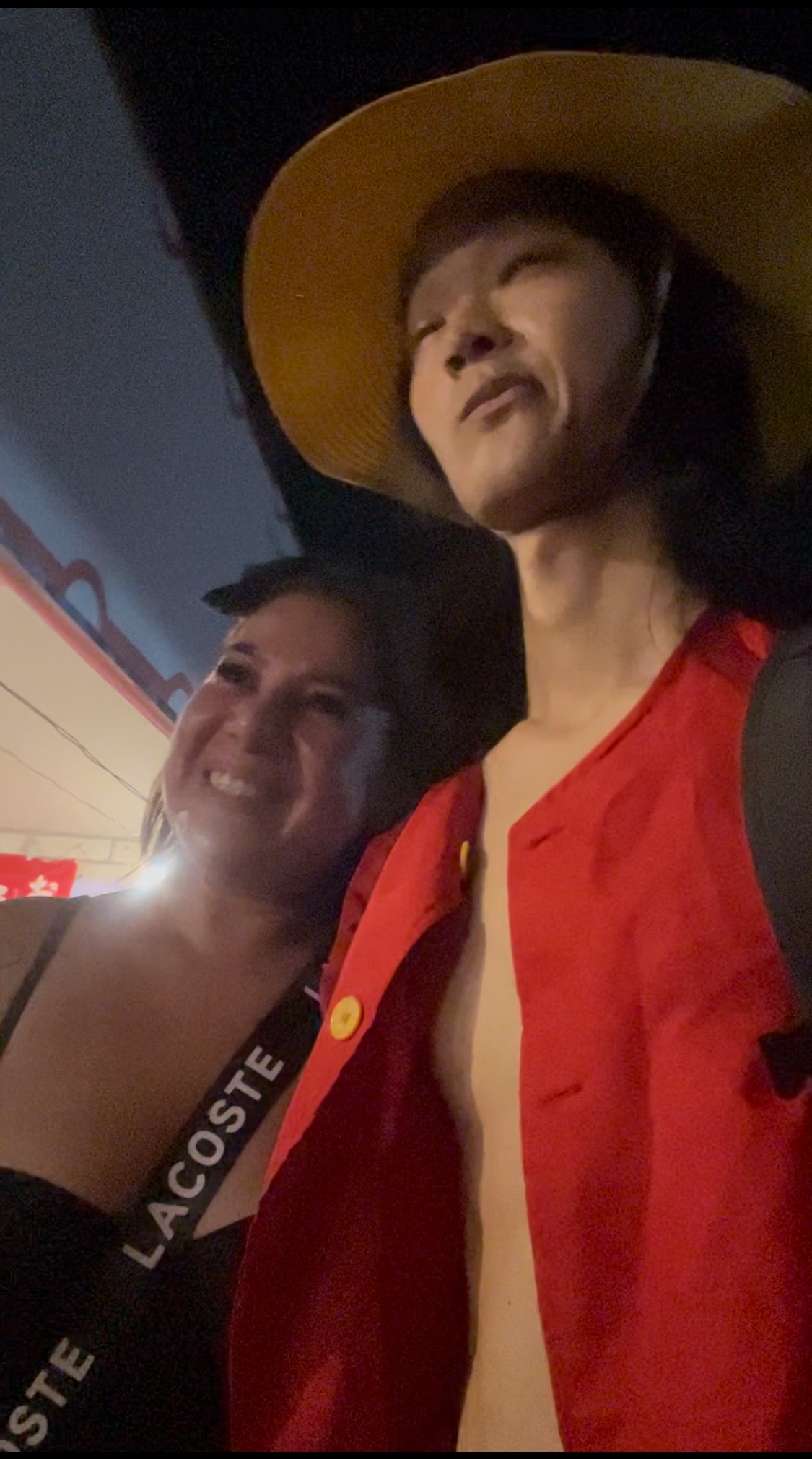 Close-up of person in straw hat looking down, festival lights in background.