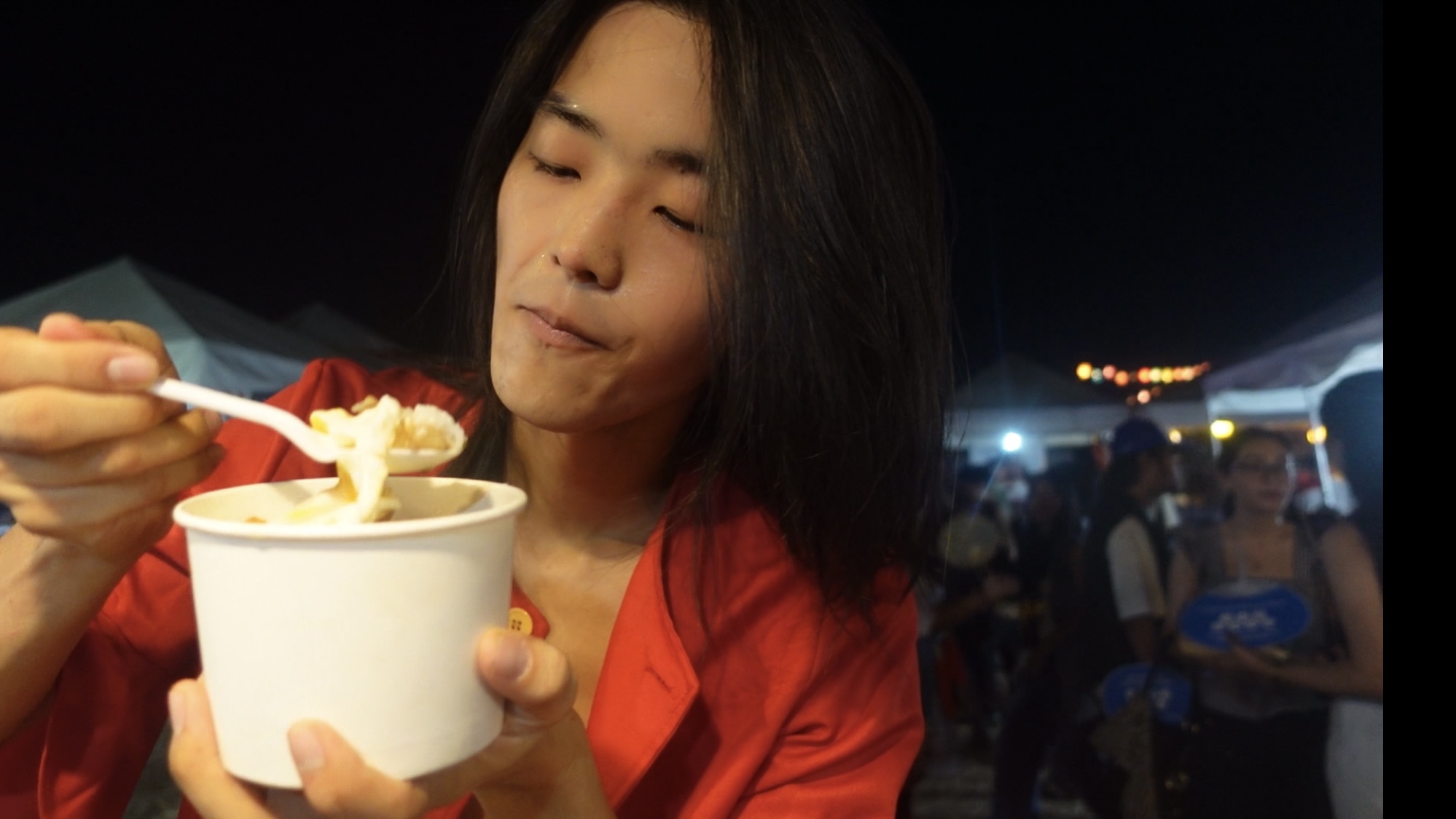 Person in red outfit eating from a white cup, looking focused.