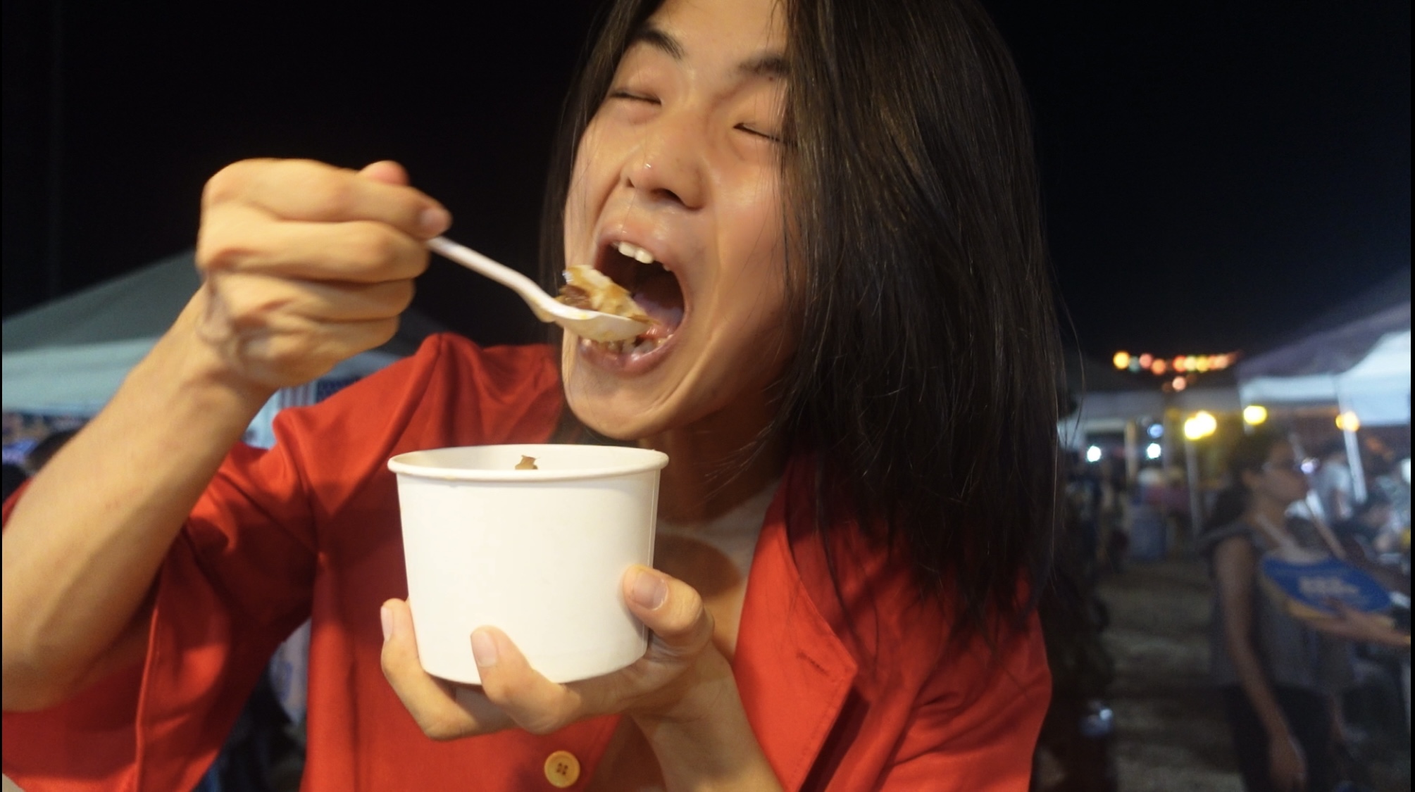 Person enjoying food from a white cup, mouth open to take a bite.
