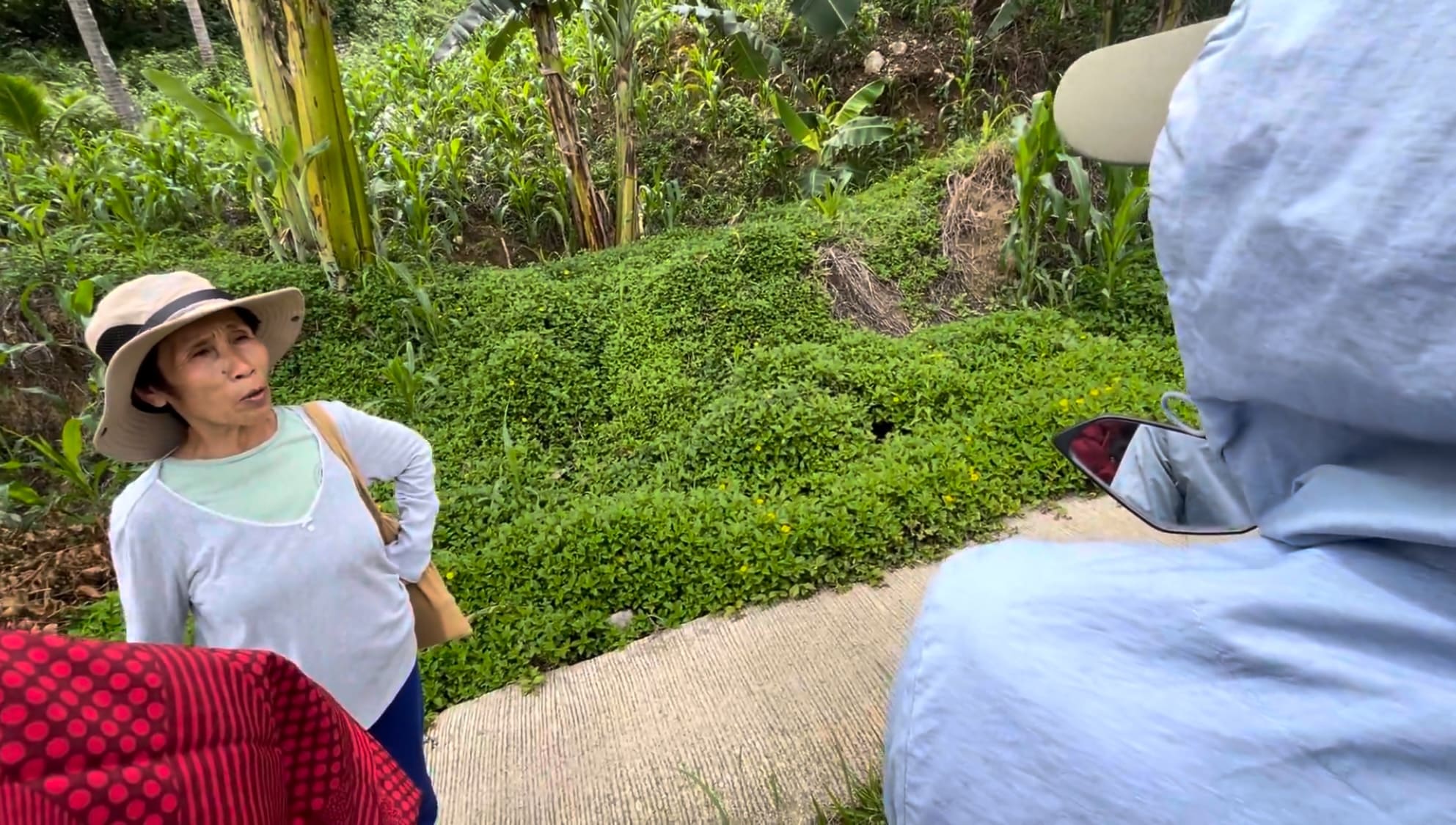 Woman and man talking beside a rough mountain road in Barangay Amancion