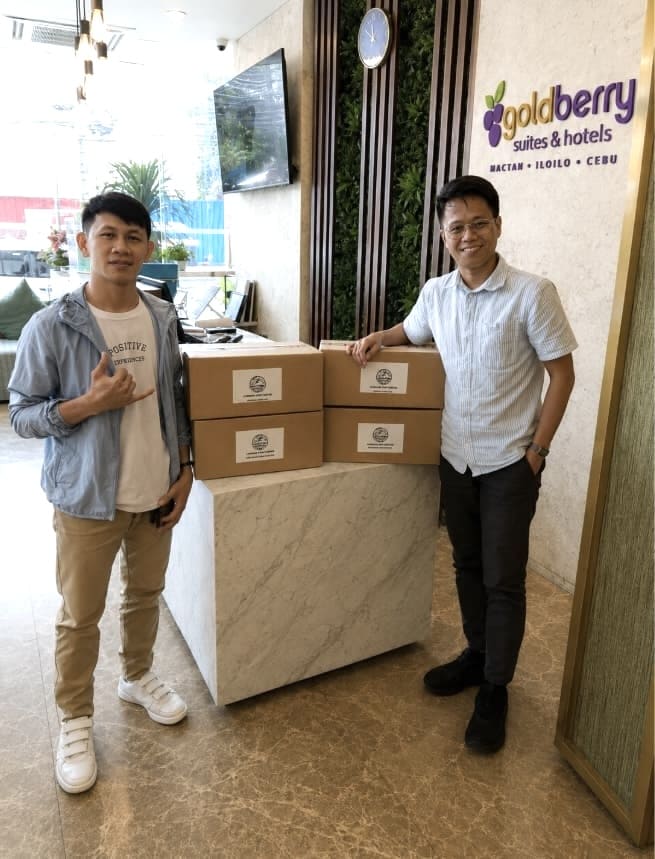 Two men posing with a cardboard box at a hotel entrance