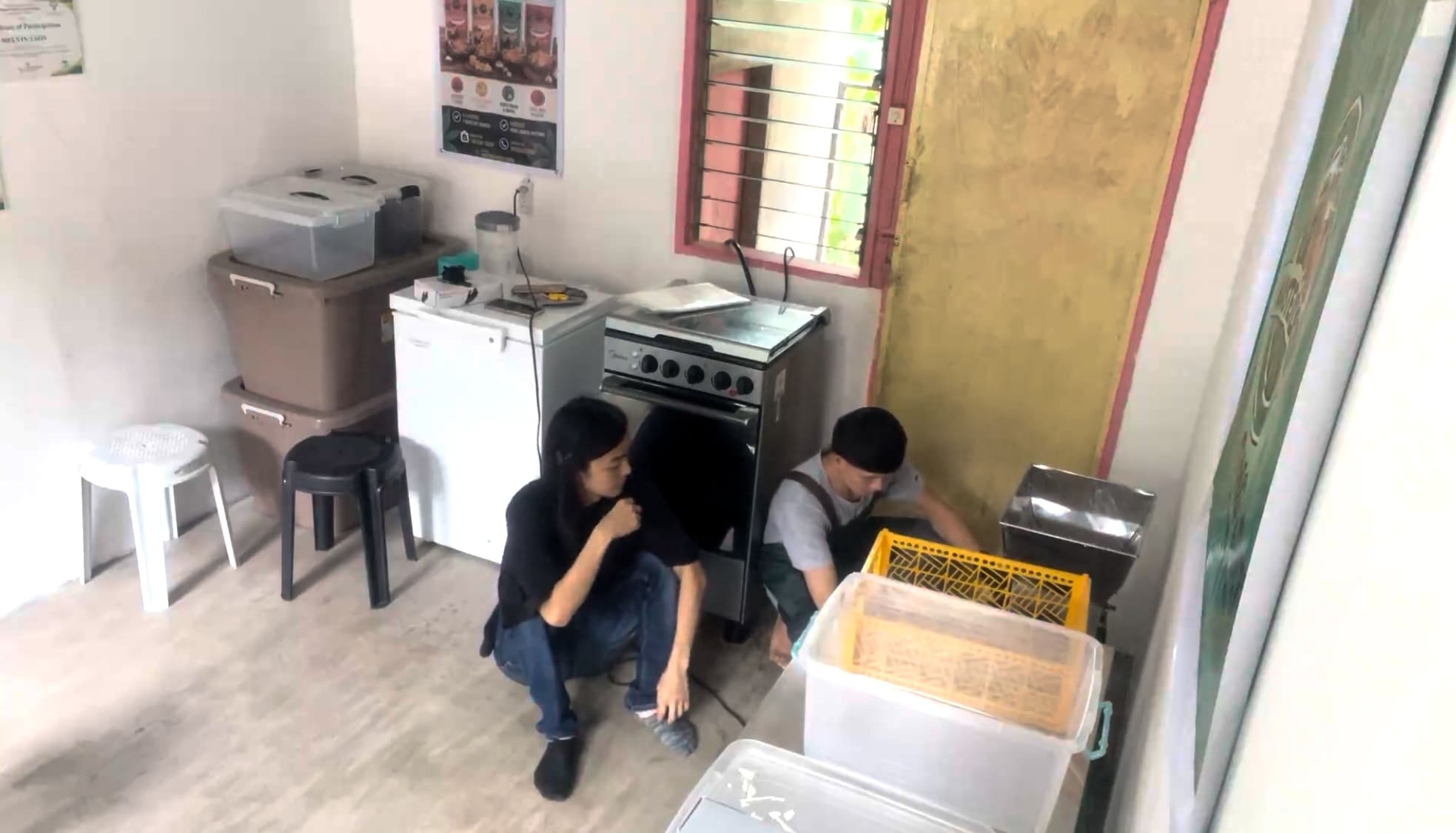 Two men standing beside a cassava grating machine
