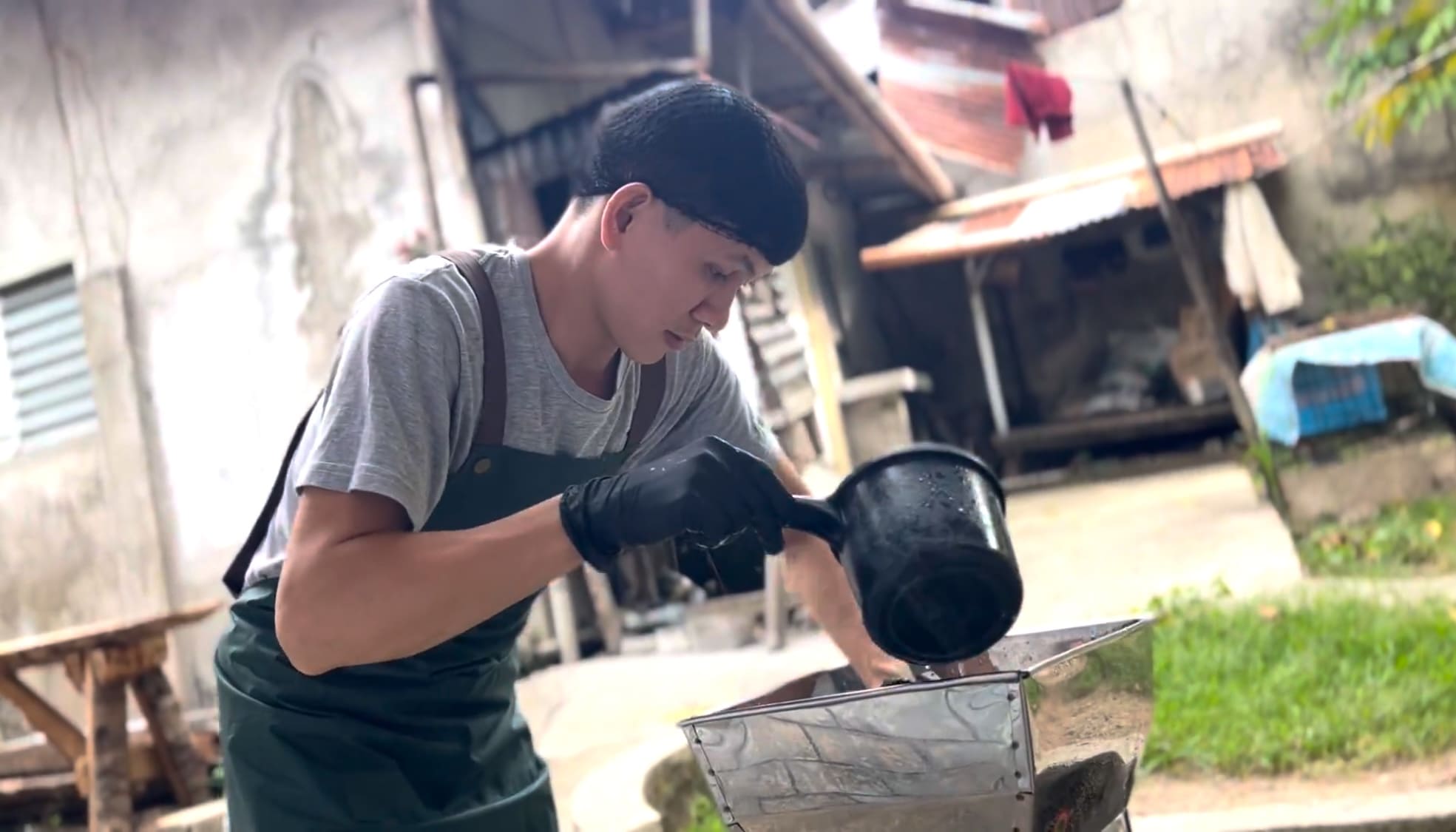 Man washing a cassava grating machine outdoors