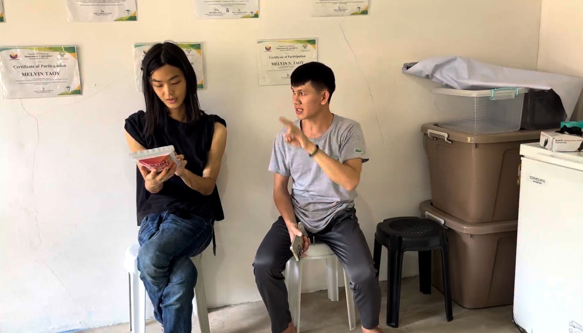 Man sitting and explaining a cassava snack product at a small processing facility