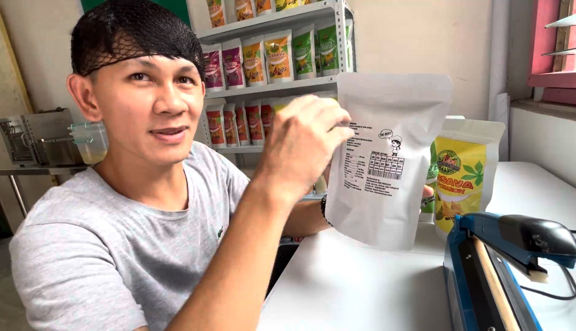 Smiling man holding a packaged cassava snack at a small processing facility