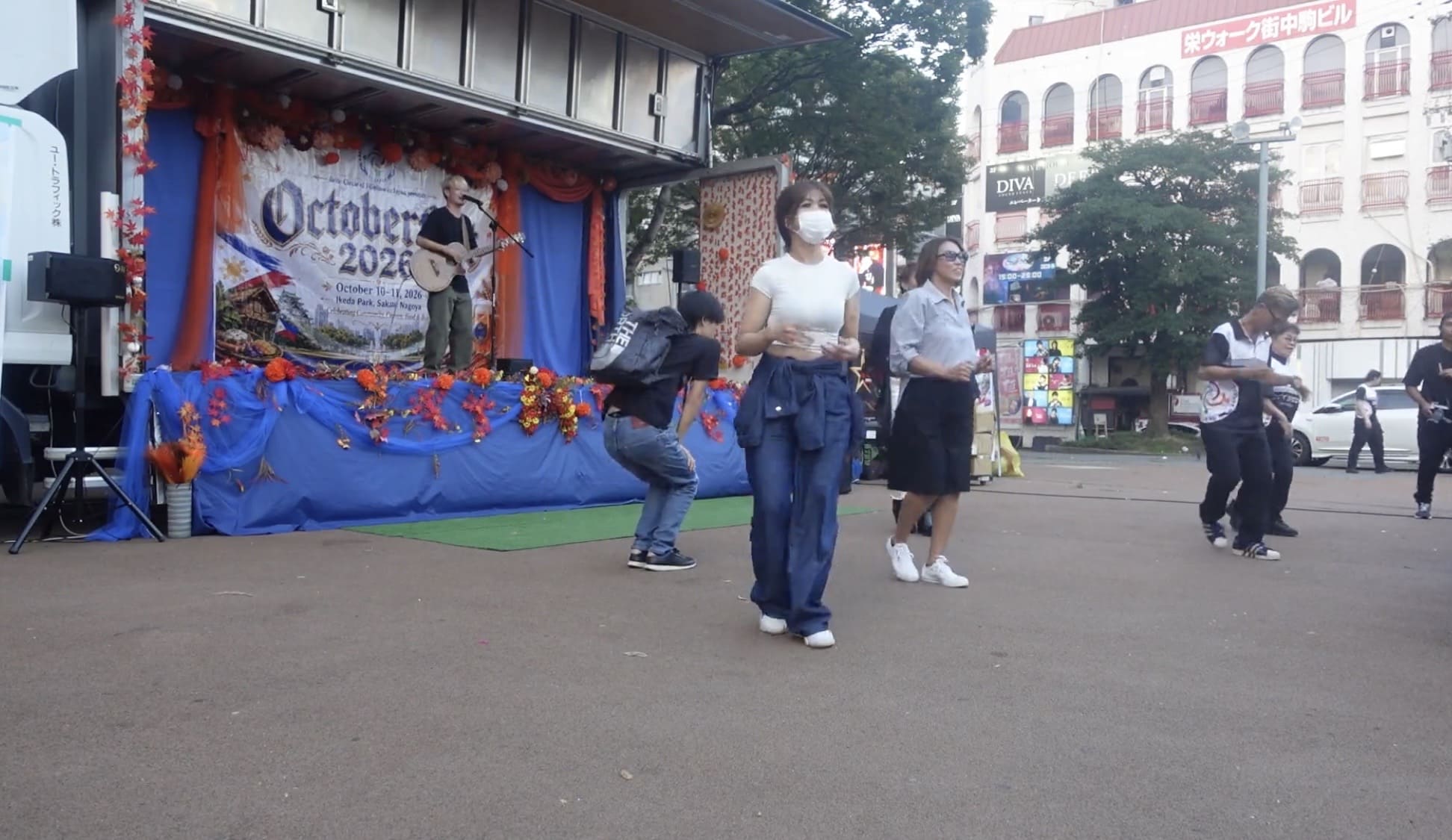 Filipino community members and Japanese attendees dancing at a cultural event with a guitarist on stage