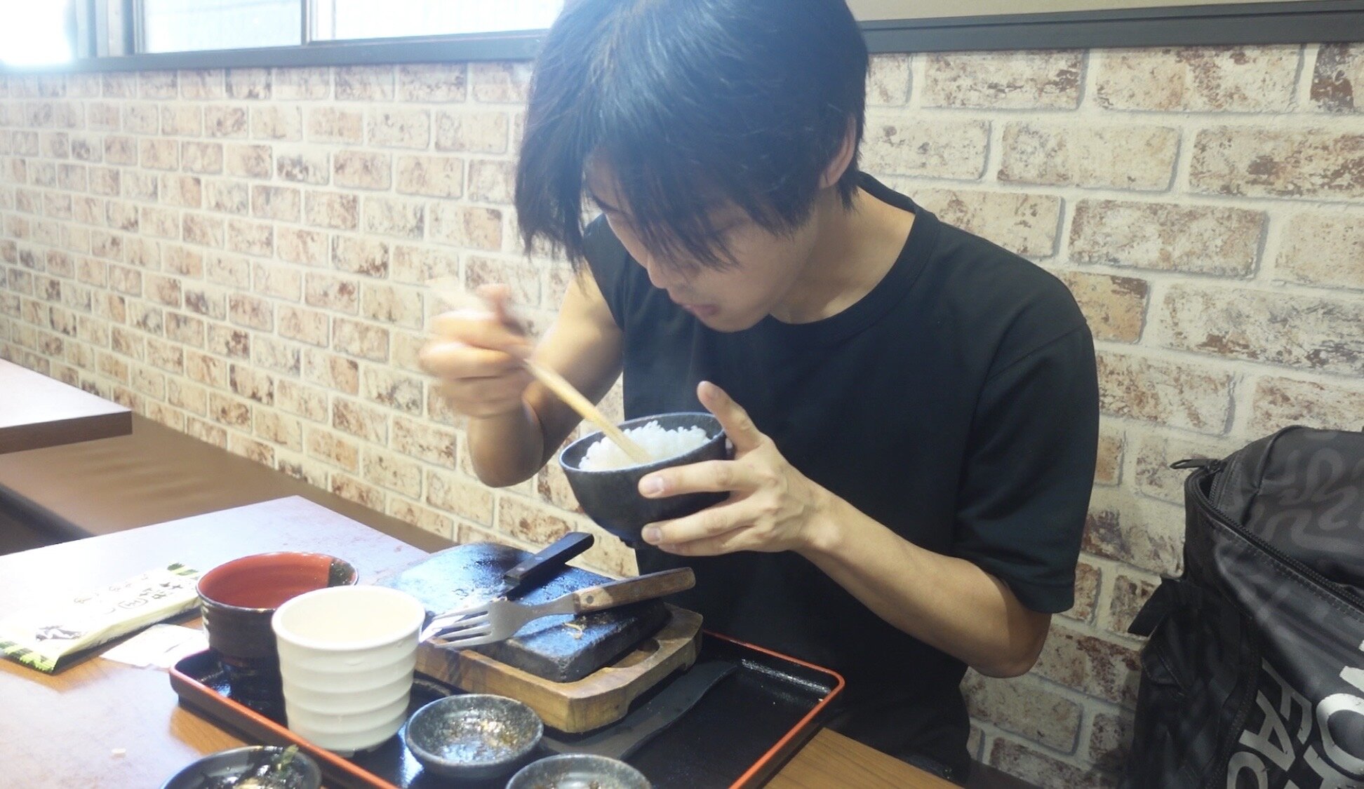A man eating meat and rice inside a restaurant